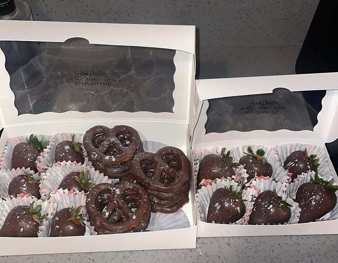 Two boxes of dark chocolate treats with shimmer dust: one mixed box of strawberries and pretzels, and one box of strawberries only, with pink-tinted liners.