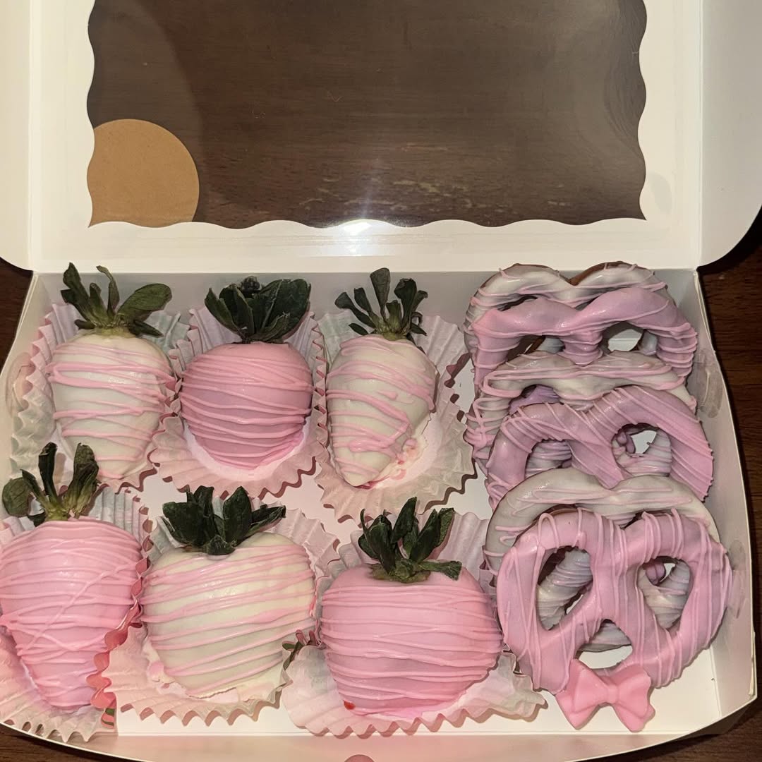 Soft pastel pink and white Valentine's box with white chocolate strawberries featuring pink drizzle and lavender-coated pretzels with a fondant pink bow.