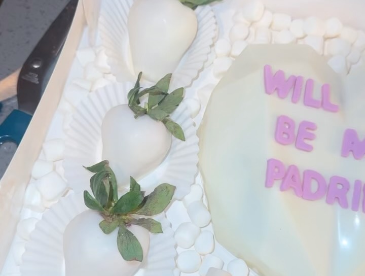 Close-up of smooth white chocolate strawberries and partial view of a breakable heart with purple padrinos lettering for a godparent proposal box.