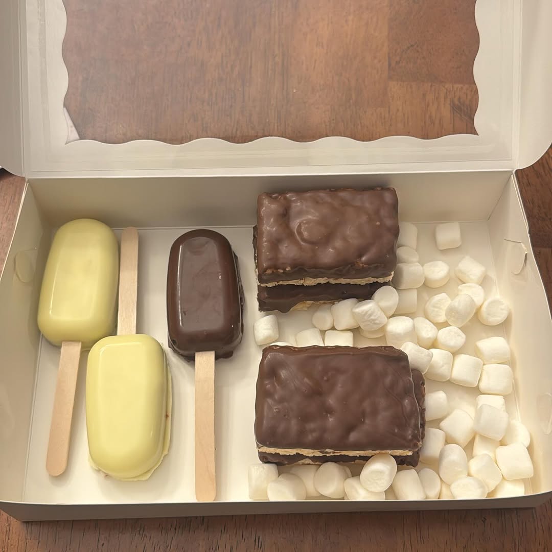 Assorted box with yellow and dark chocolate cakesicles plus layered chocolate ganache bars cushioned in mini marshmallows.