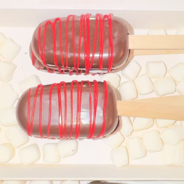 Close-up of two dark chocolate cakesicles with vibrant red drizzle lines, showcasing the glossy coating and artistic drizzle technique.