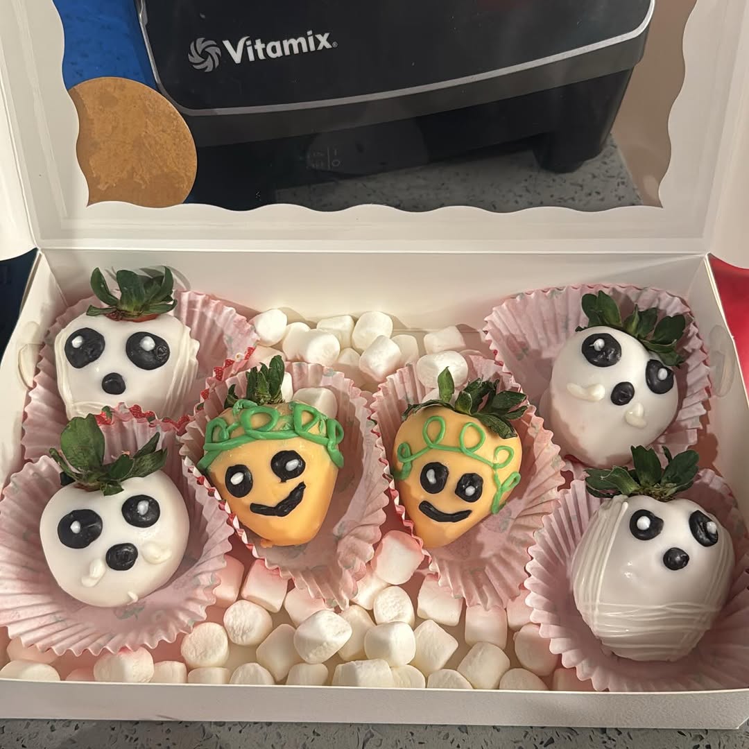 Festive Halloween box of chocolate strawberries decorated as white ghosts with smiley faces and orange pumpkins with green vines, accented with marshmallows.