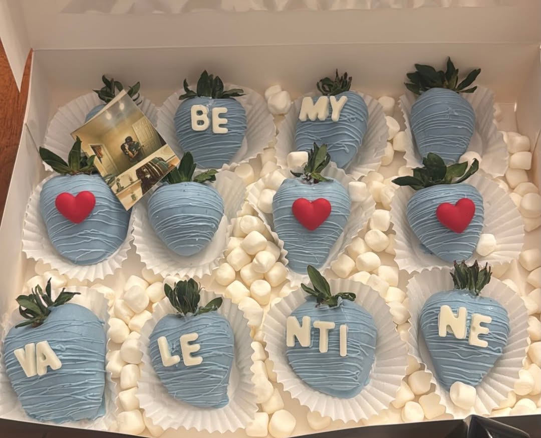 A dozen baby blue strawberries with white drizzle spelling BE MY VALENTINE in fondant letters, with red hearts and a personal photo included.